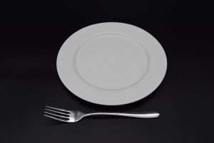 A 9" white wide rim plate next to a zephyr large fork - both available to hire near Ripon