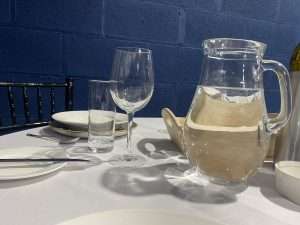 A water jug on a 4ft round table set at an event near Leeds. it is next to a large wine glass and a striaght sided water glass